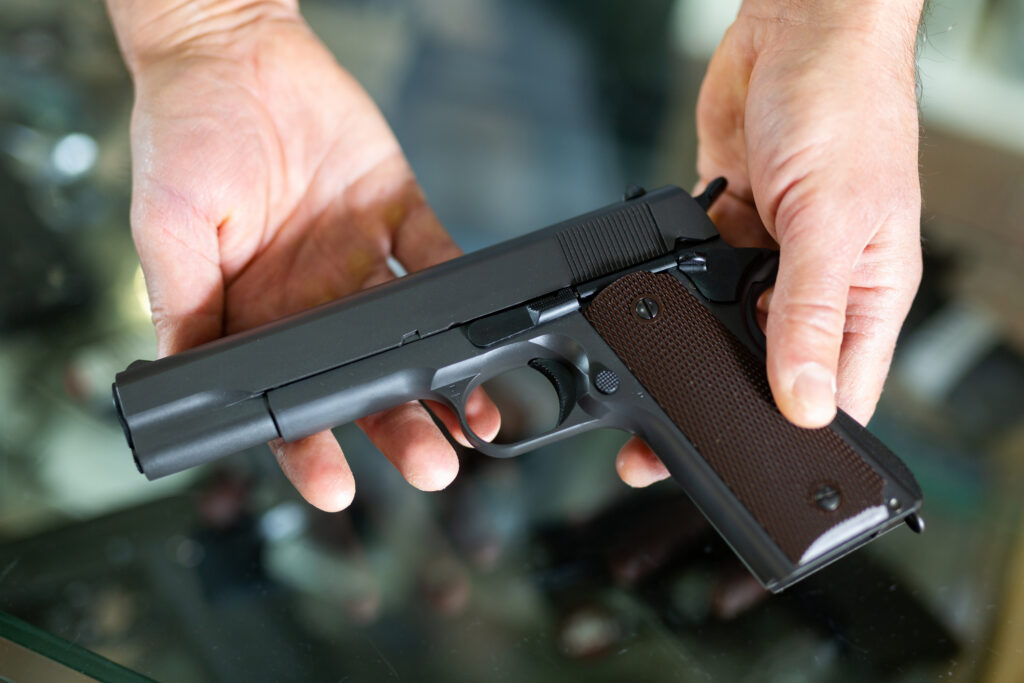 Gunsmith shop assistant demonstrates black pistol in his hands.